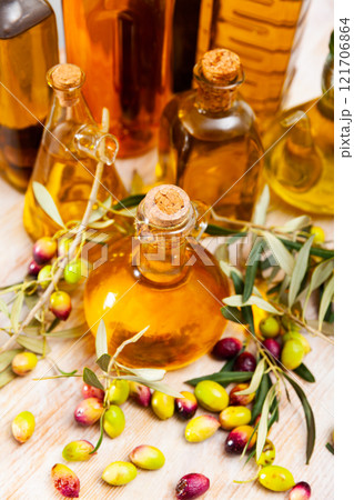 Glass bottles and carafes with fresh olive oil on wooden table with olive branches and fresh olives Glass bottles and carafes with fresh olive oil on wooden table with olive branches and fresh olives 121706864