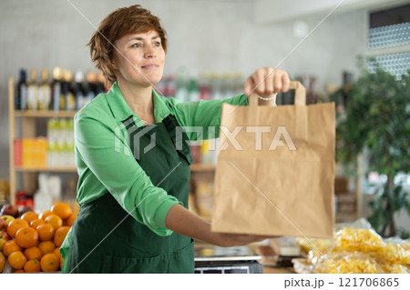 Adult woman seller with paper bag in grocery store Adult woman seller with paper bag in grocery store 121706865