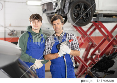 Portrait of two auto mechanics, an experienced one and student, near car in car service center Portrait of two auto mechanics, an experienced one and student, near car in car service center 121706886