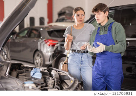Mechanic advises woman on repairs under hood of car Mechanic advises woman on repairs under hood of car 121706931