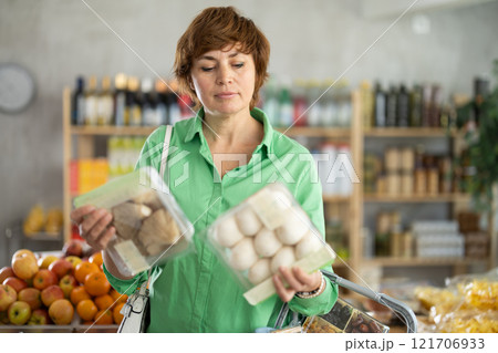 Adult woman choosing mushrooms in grocery store 121706933