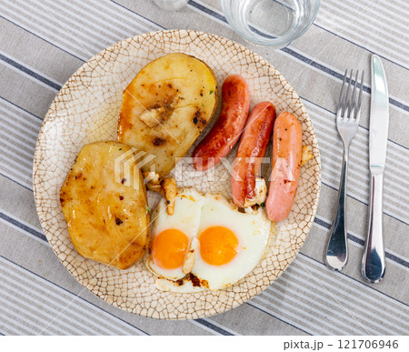 Appetizing dish of three sausages with fried eggs and potatoes 121706946