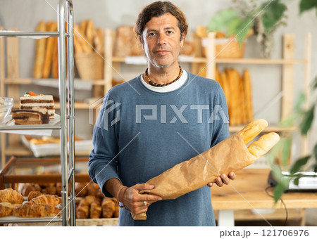 Pleased middle-aged guy holding baguettes in paper bag in bakery 121706976