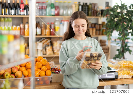 European teen girl customer at shop scans QR code on cookies package using phone camera 121707003