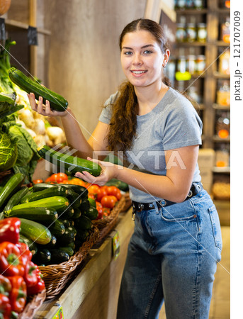 Young woman customer chooses zucchini in shop 121707009