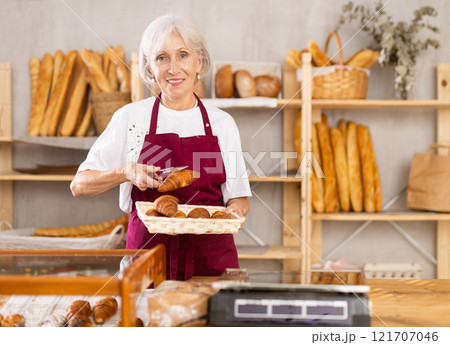 Elderly woman seller puts croissants in showcase 121707046