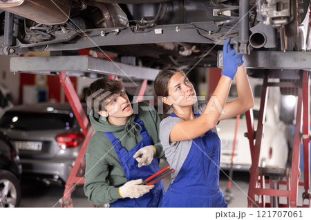 Guy and woman mechanics repairing underbody of car 121707061