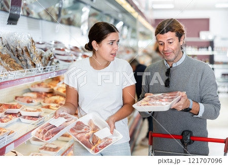 Man and woman choose fresh meat together in the meat department of supermarket 121707096