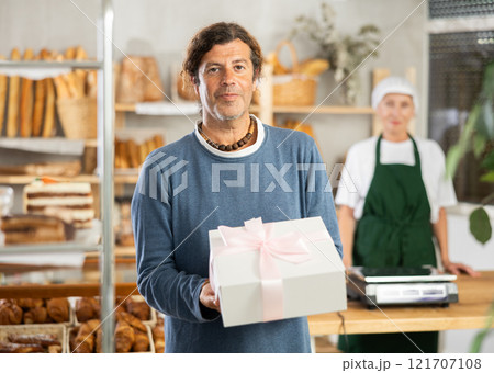Positive man bought cake in bakery, packed in white elegant box with pink bow 121707108