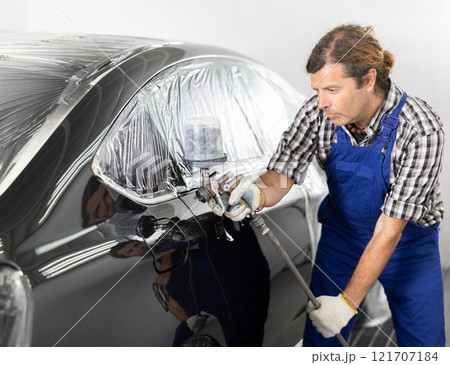 Middle aged man using spray gun to paint car in workshop Middle aged man using spray gun to paint car in workshop 121707184