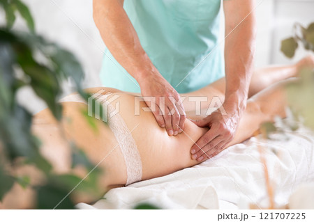 Woman covered with white towel lies and enjoys during anti-cellulite massage in hips and legs 121707225