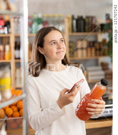European teen girl customer at shop scans QR code on grapefruit juice bottle using phone camera European teen girl customer at shop scans QR code on grapefruit juice bottle using phone camera 121707242