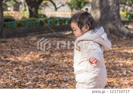 【落ち葉で敷き詰められた冬の公園で遊ぶ1歳児　立つ】 121710717