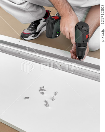 Young caucasian male assembling furniture with electric drill and screws Young caucasian male assembling furniture with electric drill and screws 121712808