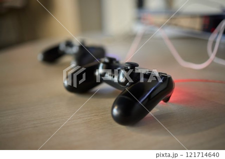 Black Gaming Controllers are placed on a Wooden Table, showcasing their modern design and style Black Gaming Controllers are placed on a Wooden Table, showcasing their modern design and style 121714640