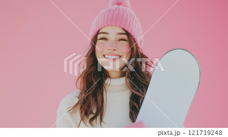 Portrait of a happy woman holding a snowboard, against a pink background. 121719248