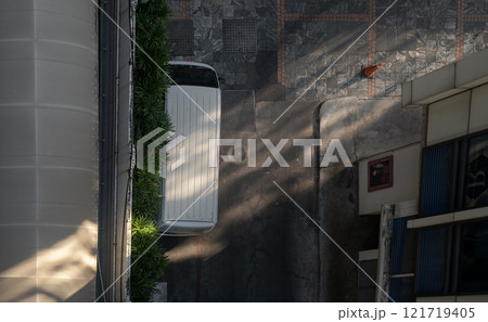 Top view of a white van parked next to a wall near a parking lot and morning light shining through. 121719405