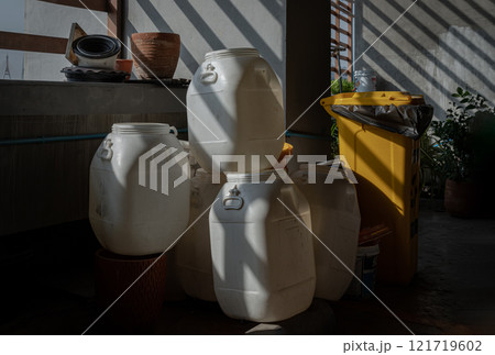 Morning sunlight shines through Wooden Battens with hitting on Gallon white plastic drums piled near the concrete wall. Morning sunlight shines through Wooden Battens with hitting on Gallon white plastic drums piled near the concrete wall. 121719602