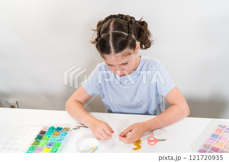 Little girl enjoys crafting colorful bracelets with vibrant clay beads set. Little girl enjoys crafting colorful bracelets with vibrant clay beads set. 121720935