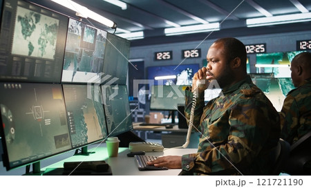 Military soldier in mission command post overseeing national safety operations, talking on phone. African american army expert in telephone call in monitoring room, camera B Military soldier in mission command post overseeing national safety operations, talking on phone. African american army expert in telephone call in monitoring room, camera B 121721190