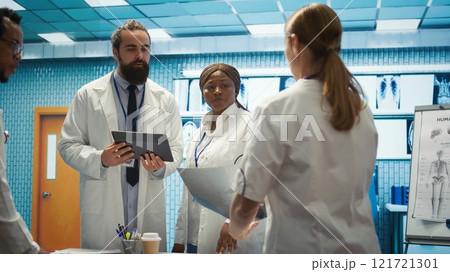 Physician and nurses reviewing medical charts and test results, aiming to deliver the best care in a hospital environment. Diverse medics consulting healthcare records for control. Camera B. 121721301