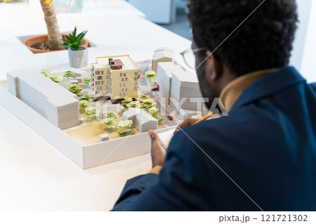 African american young architect sitting at the table and analyzing new model 121721302