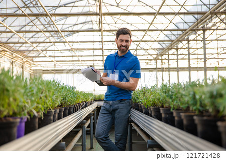 Caucasian young man working in a glasshouse and looking involved Caucasian young man working in a glasshouse and looking involved 121721428