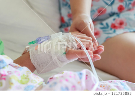 Mother holding child hand with saline IV solution in hospital Mother holding child hand with saline IV solution in hospital 121725883