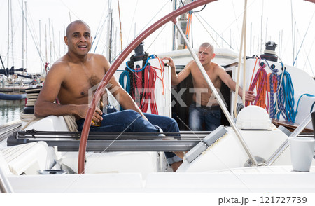 Man topless with a bottle of beer in his hand sits on the deck of a yacht in seaport 121727739