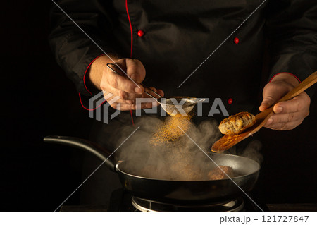 Under the warm glow of kitchen lights, a skilled chef sprinkles fragrant spices into a sizzling pan. The air fills with the enticing aromas of culinary creativity and passion at sunset Under the warm glow of kitchen lights, a skilled chef sprinkles fragrant spices into a sizzling pan. The air fills with the enticing aromas of culinary creativity and passion at sunset 121727847