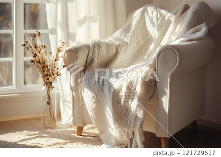 Soft white blanket elegantly laid over a cozy white armchair illuminated by gentle sunlight in a serene indoor setting 121729617