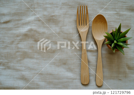 A simple table setting featuring bamboo utensils and a small succulent in a pot on a neutral fabric background A simple table setting featuring bamboo utensils and a small succulent in a pot on a neutral fabric background 121729796