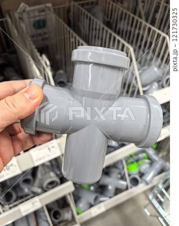 Unique gray PVC fitting held by a hand in a hardware store aisle 121730325