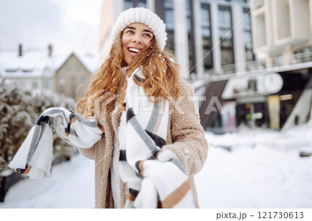 Smiling woman in a scarf and hat is having fun at street holiday fair, drinking hot drink. 121730613