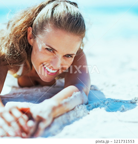 Happy young woman in swimsuit relaxing on beach 121731553