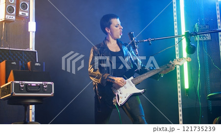 Confident musician performing live in a spotlight illuminated studio, surrounded by audio equipment and lights. Rocker doing a live performance in a rebellious style, bold attitude. Camera A. Confident musician performing live in a spotlight illuminated studio, surrounded by audio equipment and lights. Rocker doing a live performance in a rebellious style, bold attitude. Camera A. 121735239