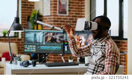 African american editor uses virtual reality glasses to do color grading, working with high tech vr headset and dual monitors at his home office. Filmmaker editing video clips. Camera B. African american editor uses virtual reality glasses to do color grading, working with high tech vr headset and dual monitors at his home office. Filmmaker editing video clips. Camera B. 121735241
