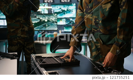 Military officer checking handguns in command room, ensuring bullets and supplies are working properly. Close up of soldier holding pistol, managing combat load equipment, camera B 121735251