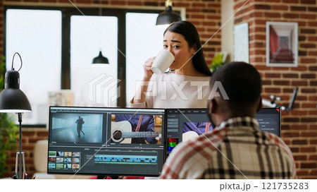 Creative team interracial partners collaborating on a video editing project, using high end video production software for color grading and mixing. Diverse couple uniting forces for work. Camera B. 121735283