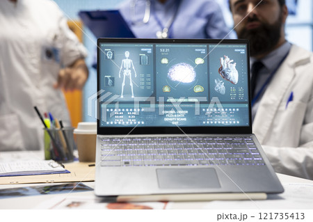 Professional staff reviews test results for potential heart condition diagnosis, looking at anatomy scan on laptop. Specialists with expertise in radiology and cardiology work on disease prevention. Professional staff reviews test results for potential heart condition diagnosis, looking at anatomy scan on laptop. Specialists with expertise in radiology and cardiology work on disease prevention. 121735413