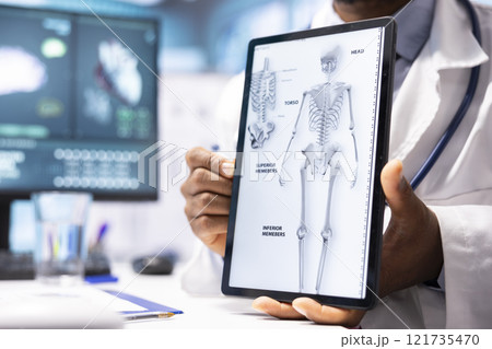 African american doctor presenting the x ray diagnostics on tablet, explaining the test results and analysis for wellness. Medical staff supporting a woman patient through recovery. 121735470