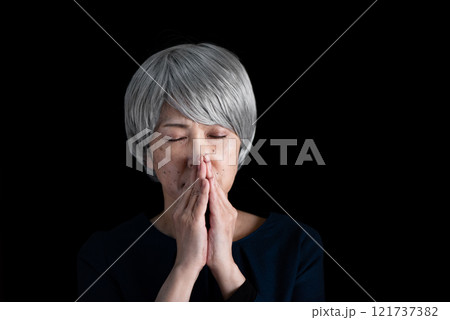 目を伏せて手を合わせるシニア女性 121737382