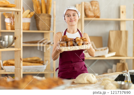 Young girl baker are standing near product range in bakery kitchen with basket loaf of croissants 121737690