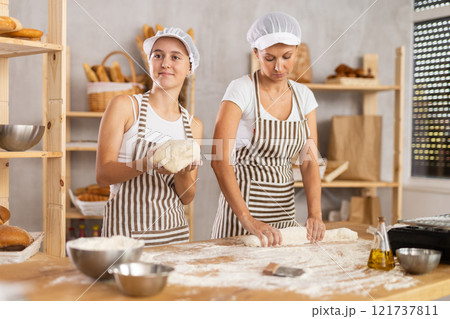 Two bakery employees work together to prepare dough for baking baguettes and croissants 121737811