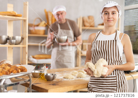 Teenage girl standing in bakehouse against baker making dough 121737816