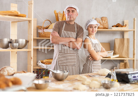 Teenage girl and male baker posing in bakehouse Teenage girl and male baker posing in bakehouse 121737825