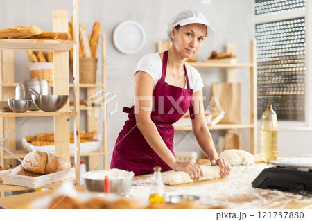 Experienced female baker shapes baguette from raw dough during baking Experienced female baker shapes baguette from raw dough during baking 121737880