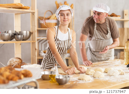 Teenage girl is kneading dough while male baker is controlling her Teenage girl is kneading dough while male baker is controlling her 121737947