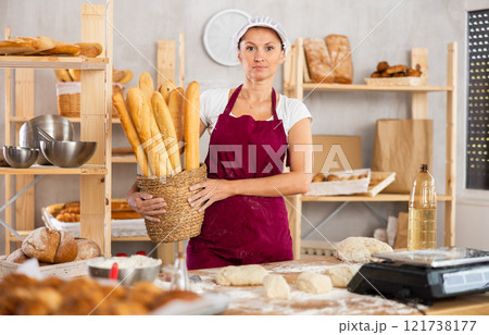 Middle-aged woman holding baguettes in round wicker basket Middle-aged woman holding baguettes in round wicker basket 121738177