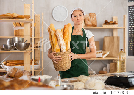 Young woman baker are standing near product range in bakery kitchen with basket loaf of baguettes 121738192